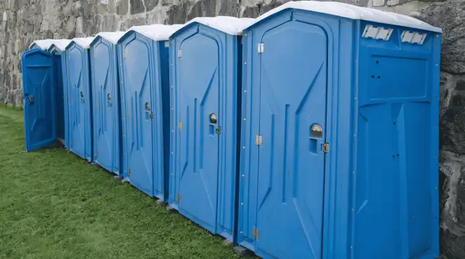 Row of blue portable toilets lined up on grass against a stone wall for event sanitation in Irvine, CA