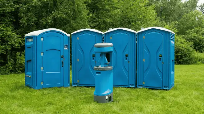 Four blue portable toilets and a matching hand washing station on grass near trees, a common sight at local outdoor events in Irvine, CA
