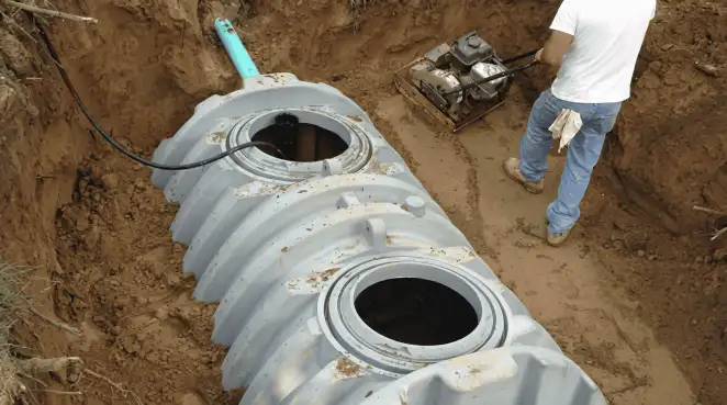 Septic tank installation showing a technician compacting soil around a new poly septic tank in an excavation pit in Irvine, CA